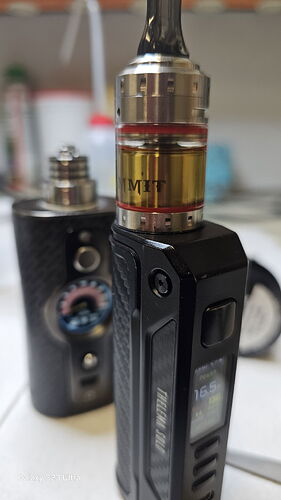 Az képen egy fekete színű vape eszköz látható, melynek a tartályában sárgás folyadék található. (Feliratozva AI-val)