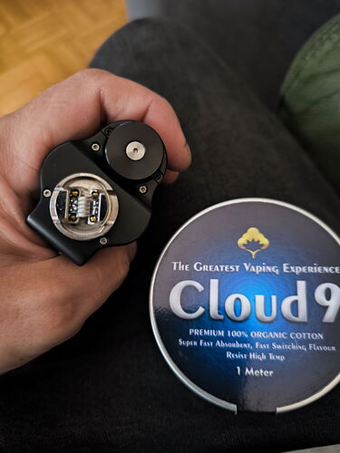 Egy kéz tart egy nyitott gőzölő készüléket, mellette egy doboz "Cloud 9" organikus pamut található. (Feliratozva AI-val)