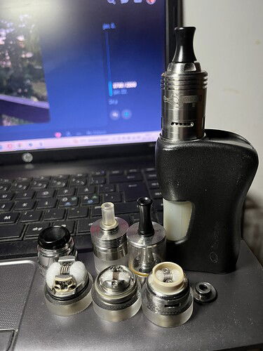 Egy fekete vaporizer és több különböző porlasztó alkatrész egy laptop billentyűzetén vannak elhelyezve. (Feliratozva AI-val)