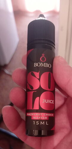 Egy kéz tart egy fekete palackot "Bombo Solo Juice Hazelnut Choco Waffer 15 ML" felirattal. (Feliratozva AI-val)