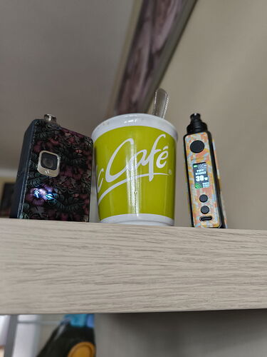 Két vape eszköz és egy sárga kávéscsésze látható egy világos fából készült polcon. (Feliratozva AI-val)