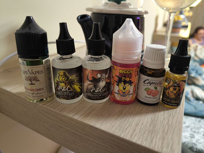 Hat különböző e-liquid palack sorakozik egy fa polcon, homályos háttérben egy üveg és egy személy látható. (Feliratozva AI-val)