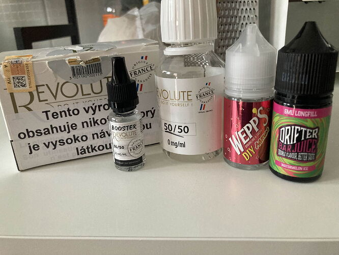 Több üveg és egy doboz Revolute márkájú e-liquid és gőzölési kellék van elrendezve egy fehér felületen. (Feliratozva AI-val)