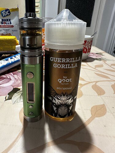 Egy zöld vape eszköz áll egy nagy üveg GUERRILLA GORILLA e-liquid mellett egy asztalon. (Feliratozva AI-val)