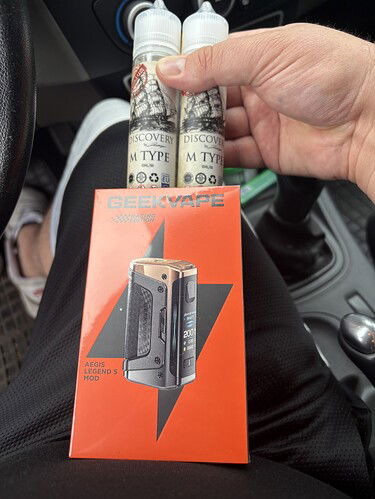 Egy személy két üveg e-liquidet és egy Geekvape vaping eszköz dobozát tartja. (Feliratozva AI-val)
