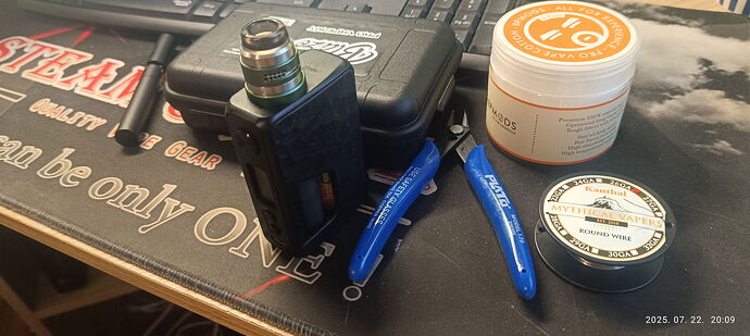 Egy asztalon elhelyezett e-cigaretta felszerelés látható, mely magában foglal egy vape modot, kék fogókat, tekercselt huzalt és vattát. (Feliratozva AI-val)