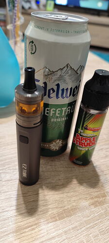 Egy EZ Tube e-cigaretta, egy doboz Edelweiss sör és egy almastrudel ízesítésű e-liquid látható egy asztalon. {tags: e-cigarette, beer, e-liquid} (Feliratozva AI-val)