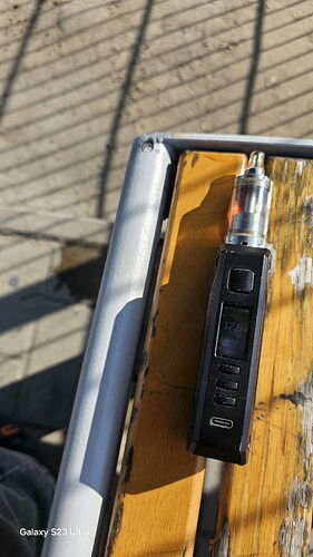 Egy fekete vape eszköz fekszik egy fa padon, napfényben. (Feliratozva AI-val)