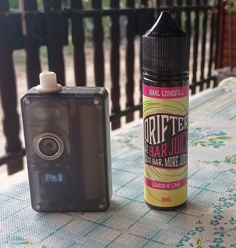 Egy sötétszürke gőzölő eszköz áll egy citrom és lime ízű Drifter Bar Juice e-liquid flakon mellett egy mintás asztalon. (Feliratozva AI-val)
