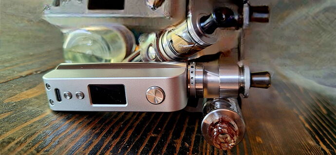 Egy asztalon fém és üveg részekből álló elektronikus cigaretta vagy vape eszköz látható közeli képen. (Feliratozva AI-val)