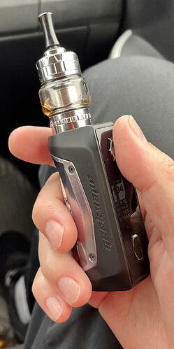 Egy kéz egy fekete Geek Vape elektronikus cigarettát tart. (Feliratozva AI-val)
