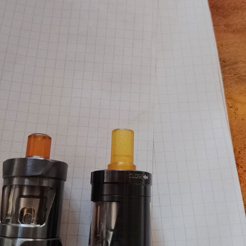 Két vape eszköz narancssárga és sárga szájrésszel látható egy rácsos papíron elhelyezve. (Feliratozva AI-val)
