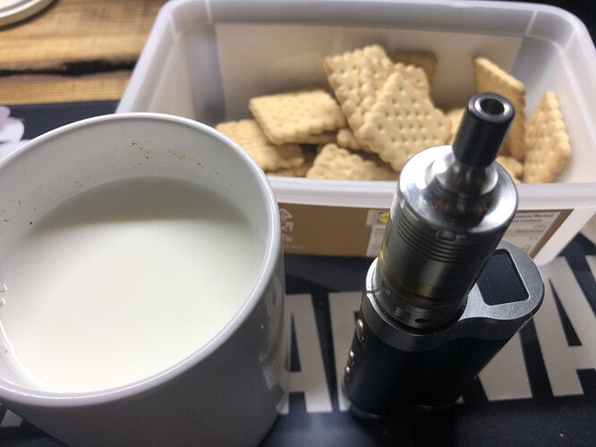 Egy bögre tej, egy e-cigaretta és egy doboz keksz látható a képen. {tags: food, drink, vaping, snacks} (Feliratozva AI-val)