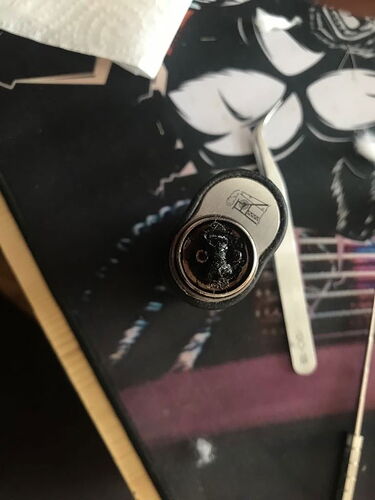 Az képen egy elégett vagy sérült mikrofonszélvédő látható egy asztalon, amely mellett egy csipesz is fekszik. (Feliratozva AI-val)