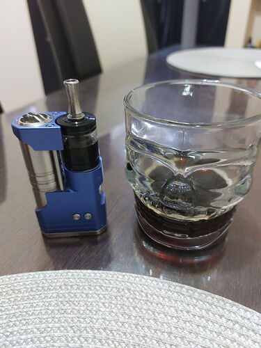 Egy kék színű gőzölő készülék és egy pohár sötét ital van az asztalon. (Feliratozva AI-val)