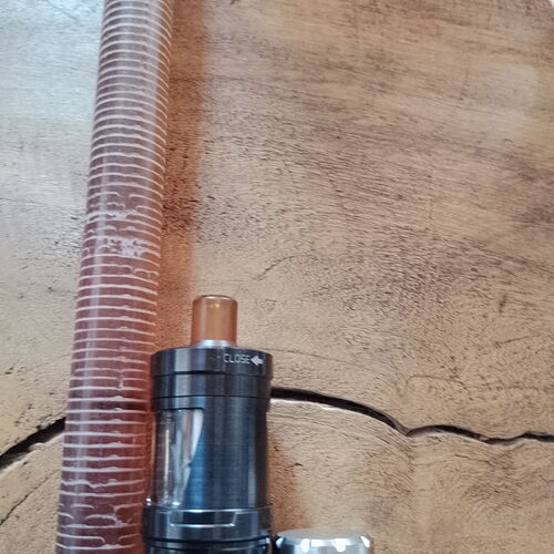 Egy sötét színű vape eszköz borostyánsárga szájrésszel és egy átlátszó bordázott cső fekszik egy fa felületen. (Feliratozva AI-val)