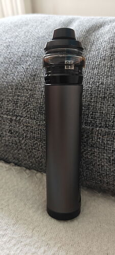 Egy fekete színű elektornikus cigaretta vagy vape eszköz egy szürkéskék háttér előtt van elhelyezve. (Feliratozva AI-val)