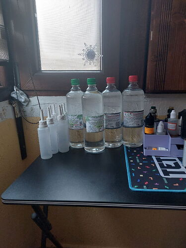 Az asztalon négy üveg ásványvíz és néhány üres spray üveg található, mellette különböző kozmetikumok. (Feliratozva AI-val)