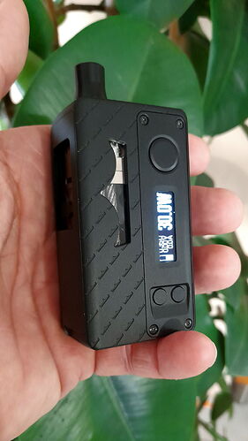 Egy kézben tartott, feketés elektronikus cigaretta vagy vape eszköz látható, amelyen digitális kijelző és vezérlőgombok vannak. (Feliratozva AI-val)