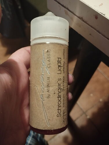 Egy kéz egy üveget tart, amelyen a "Schrodinger's Liquid" felirat olvasható, és a címkén barna papír található. (Feliratozva AI-val)