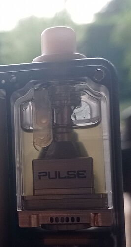 Egy e-cigaretta folyékony tartályának közelképe látható, melyen a „PULSE” felirat olvasható, áttetsző fallal, melyen keresztül látszik a sárgás folyadék és a belső mechanika. (Feliratozva AI-val)