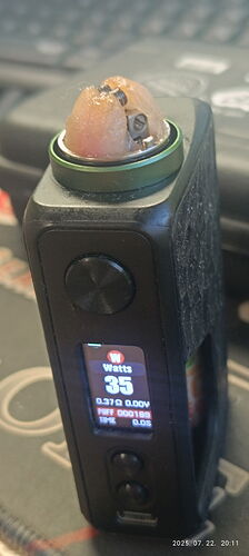 Egy fekete vape eszköz látható, melynek kijelzője 35 wattot mutat, tetején pedig egy tekercs és nedvszívó anyag van. (Feliratozva AI-val)