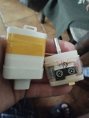 Két elektronikus alkatrészt tartanak egy kézben, az egyik sárga és fehér, a másik pedig átlátszó, belső részekkel. (Feliratozva AI-val)