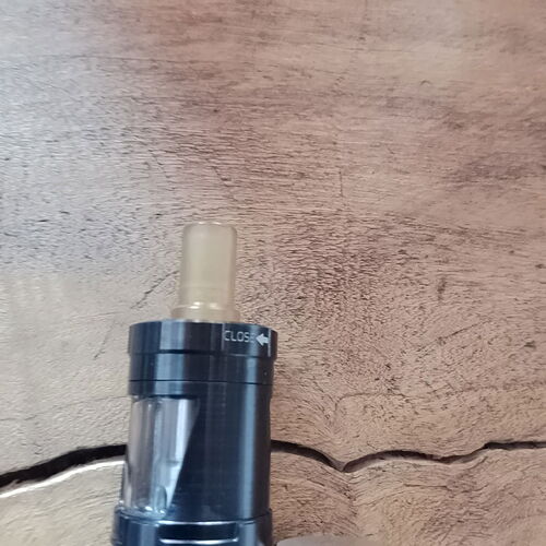 Egy fekete vape készülék átlátszó felső résszel egy fa felületen látható. (Feliratozva AI-val)