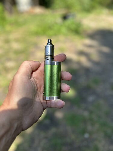 Egy kéz tart egy zöld színű vape eszközt a szabadban. (Feliratozva AI-val)