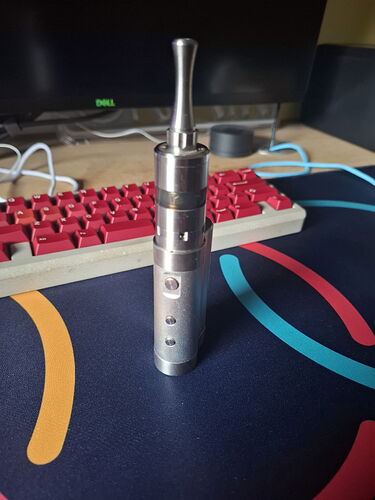 Egy ezüst színű, henger alakú e-cigaretta állítólag a számítógépes billentyűzet előtt egy asztalon. (Feliratozva AI-val)