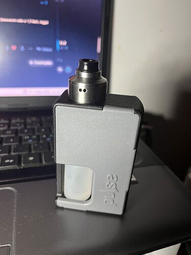 Egy szürke, 'Pulse' feliratú vape készülék áll egy fekete laptop billentyűzetén, háttérben a bekapcsolt képernyővel. (Feliratozva AI-val)