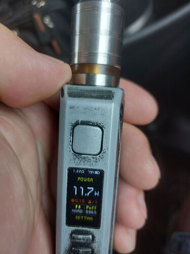 Egy kéz tart egy szürke elektromos cigarettát, amelynek kijelzőjén 11.7W látható. (Feliratozva AI-val)