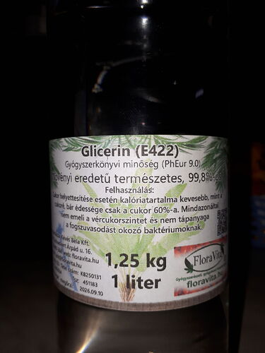 A képen egy üveg glicerin (E422) címkéje látható, amely 99,8%-os természetes eredetű és gyógyszerkönyvi minősítéssel rendelkezik, 1,25 kg tömegű és 1 literes kiszerelésben. (Feliratozva AI-val)